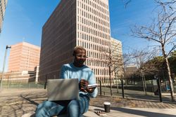 Stylish young Black man working remotely on laptop in city park