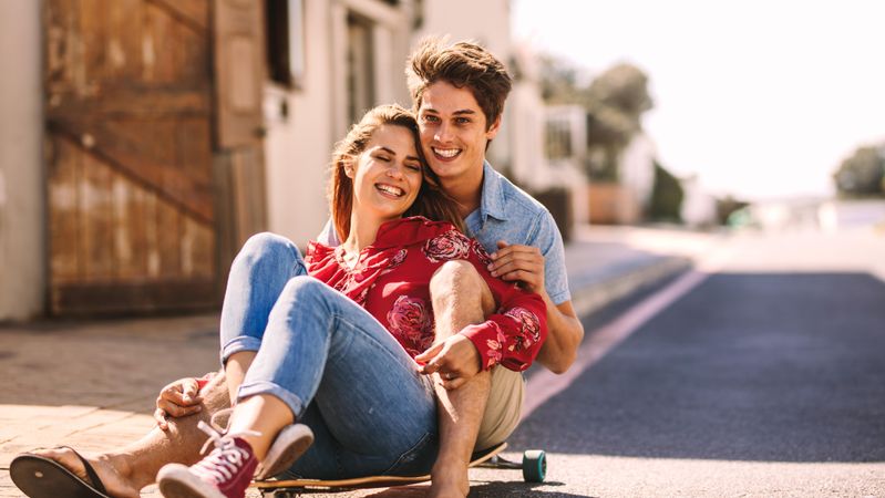 Man sitting on a skateboard with a woman enjoying a ride outdoors