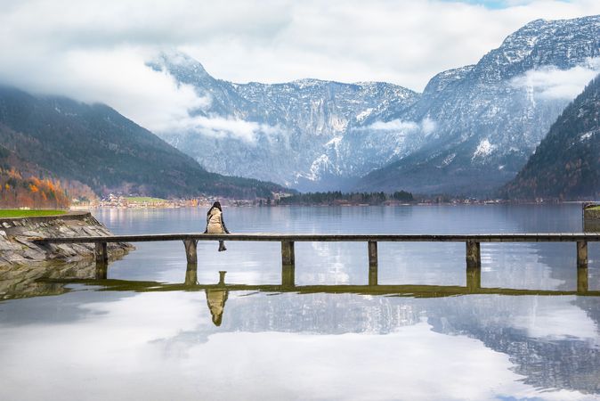 Woman sitting on bridge over beautiful lake with mountains behind