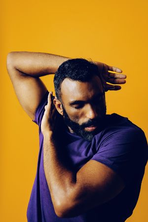 Black man in yellow studio with arms surrounding his head, vertical composition