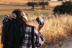 Young woman taking photos with analog camera in the field at sunset