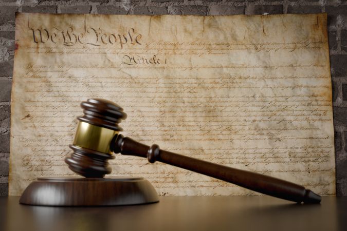 United States Constitution On Wall with Gavel Resting on Table in Front.
