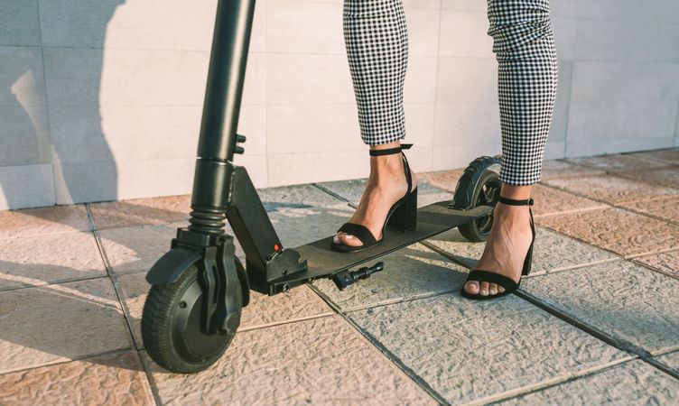 Unrecognizable businesswoman legs with e-scooter outdoors