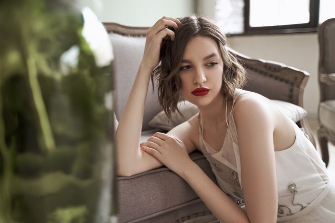 woman with red lips in white dress looking away while sitting on floor beside sofa