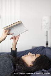 Young woman laying in bed reading a book 4BgBXb