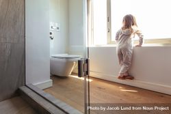 Little girl in bathroom standing by a big window and looking outside 5kmwWb