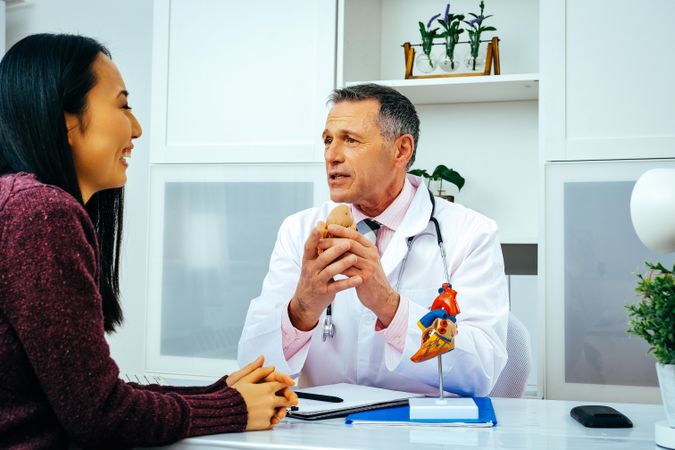 Male doctor with smiling female patient consulting about heart structure