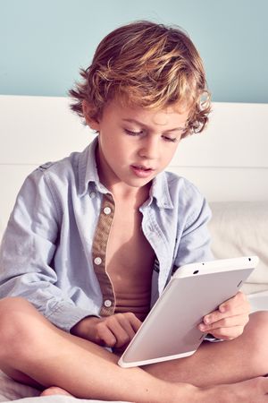 Serious boy using tablet on bed