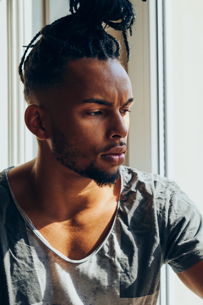 Thoughtful Black male sitting on windowsill