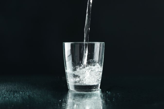 Dark room with single glass of water being poured, copy space