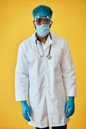 Portrait of Black male doctor in yellow studio with full ppe gear ready for surgery