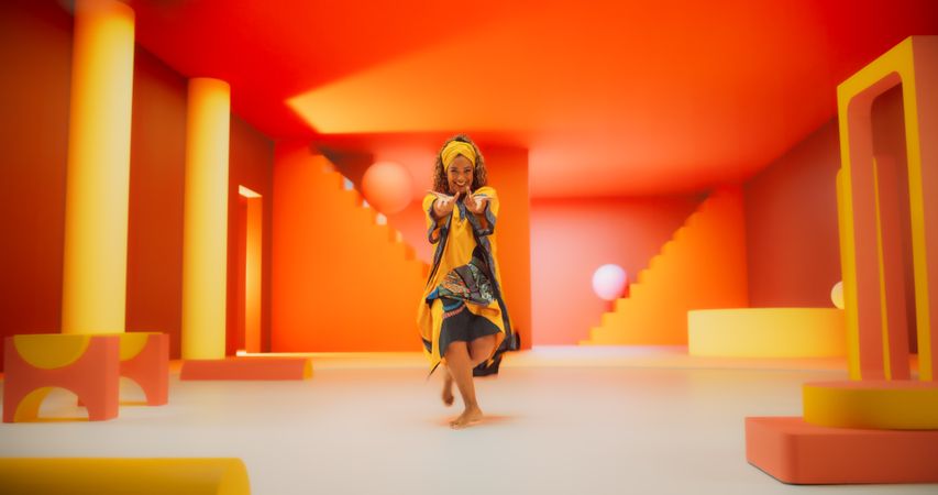 Black Woman in African Outfit Dancing Energetically in Geometric Abstract Orange Environment. Creative Female Performing Dance Choreography in a Studio, Making Moves, Having Fun.