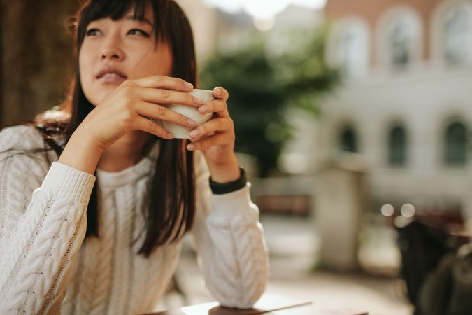 Close up of woman’s hands holding coffee outside with woman behind
