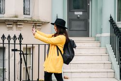 Stylish woman using smartphone near house on street