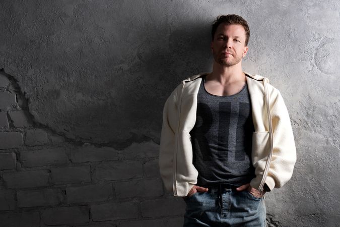 Man in fleece hoodie and jeans leaning against wall.