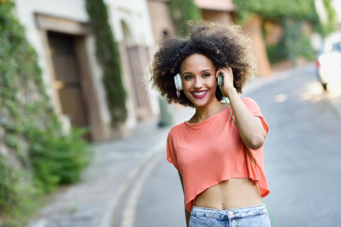 Carefree woman walking down the street wearing orange t-shirt and blue jeans with afro hairstyle