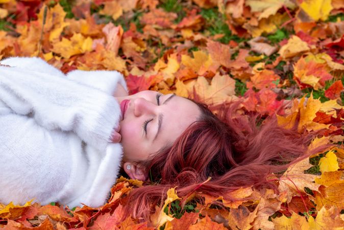 Woman lying in autumn leaves with eyes closed