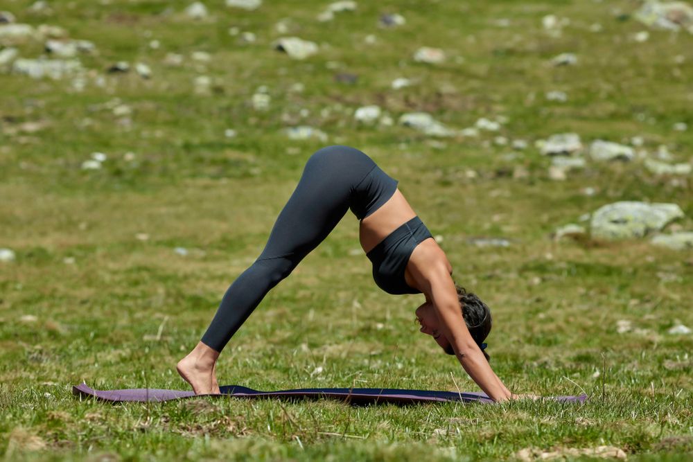 Woman in gray yoga outfit doing downward dog pose with bare feet in a mountain valley
