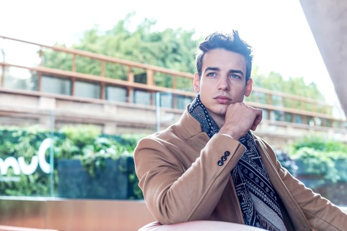 Contemplative man wearing winter clothes looking around sitting on a leather bench outside