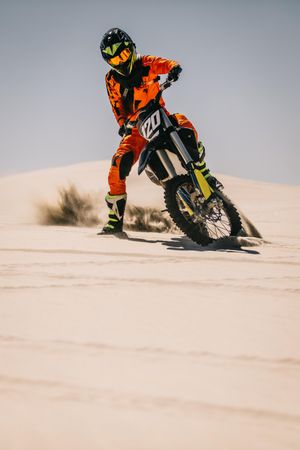 Motocross bike rider riding over sand dune