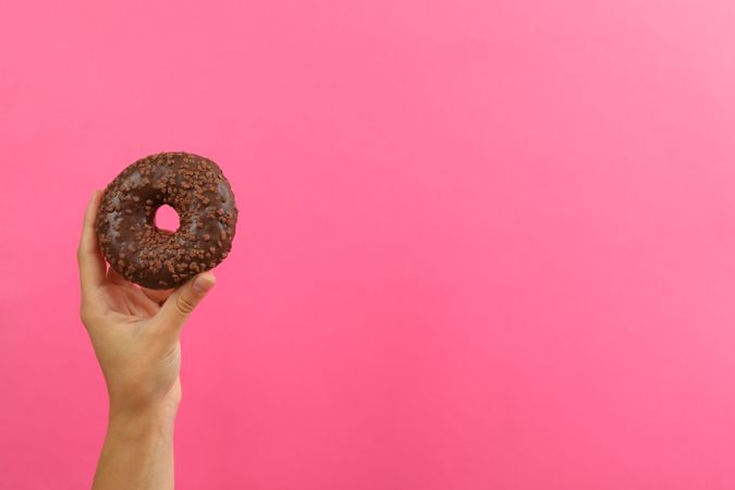Female hand hold tasty donut on pink background