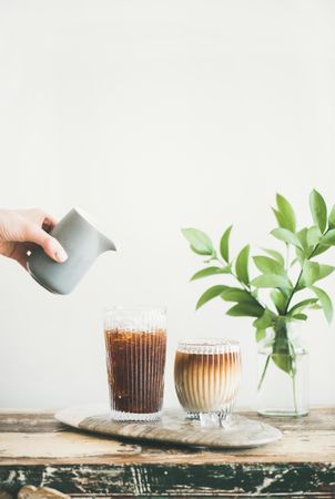 Hand pouring cream into iced coffee, copy space