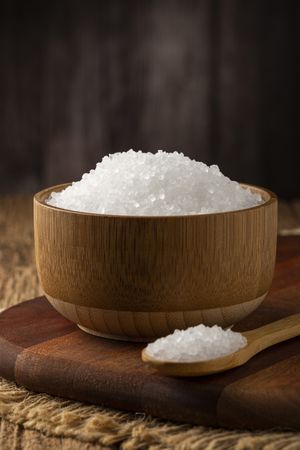 Coarse salt in bowl on wooden background.