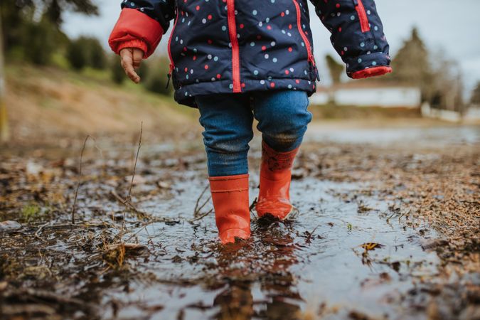 A child in rain boots walking through a puddle