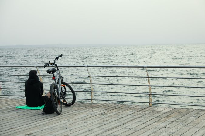 Man with bicycle on wooden floor at sea, space for text