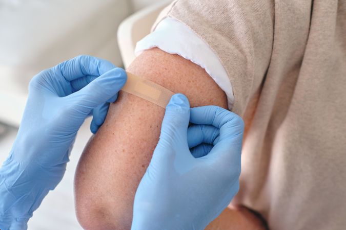 Crop nurse applying medical plaster on arm of patient
