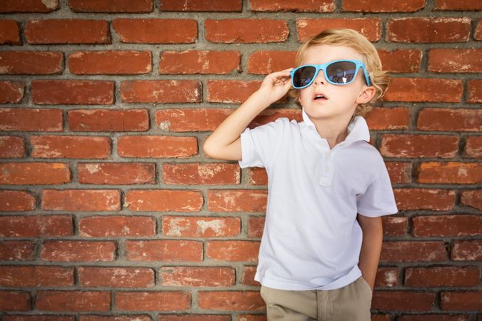 Cute Young Boy Wearing Sunglasses Against Brick Wall