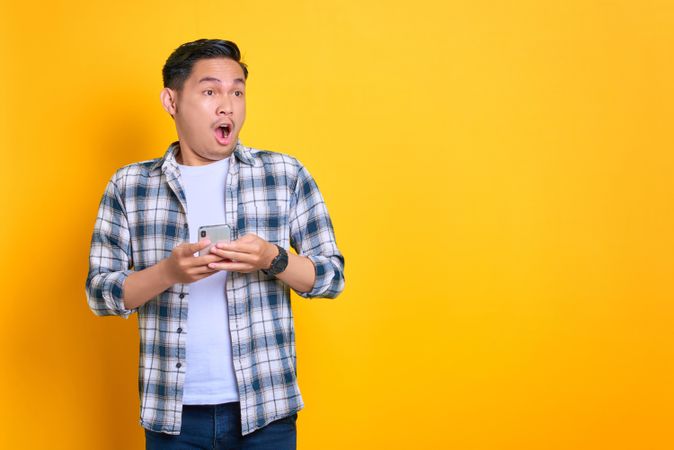 Surprised Asian male with his phone in studio shoot with copy space