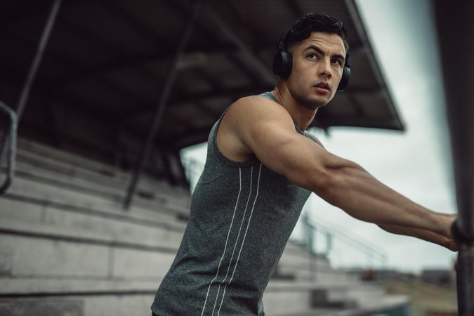 Fit young man in sportswear wearing headphones listening to music during outdoor training