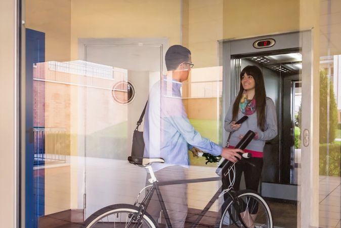 Businessman and sportive woman waving behind glass