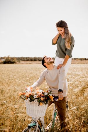 Playful lovers riding bicycle on wheat field
