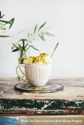 Cup of pistachio ice cream with spoon sticking upright with leaves on light background bGEwX5