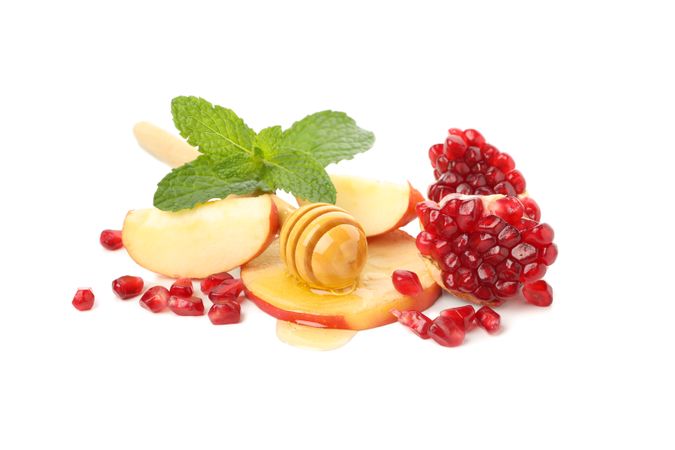 Honey dipper, pomegranate seeds, mint, and apple centered on plain table