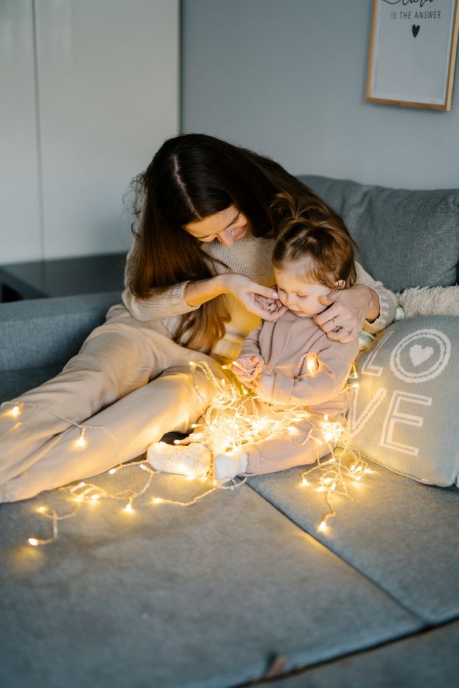 Mother and baby sitting on bed and playing with string light