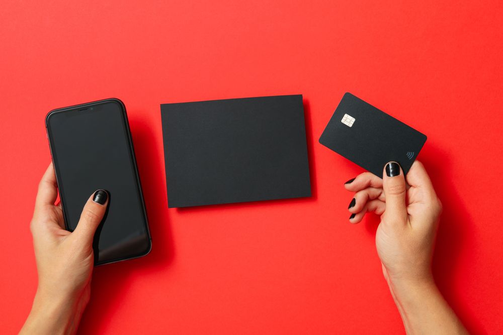 Female hands hold phone and card on red background, space for text