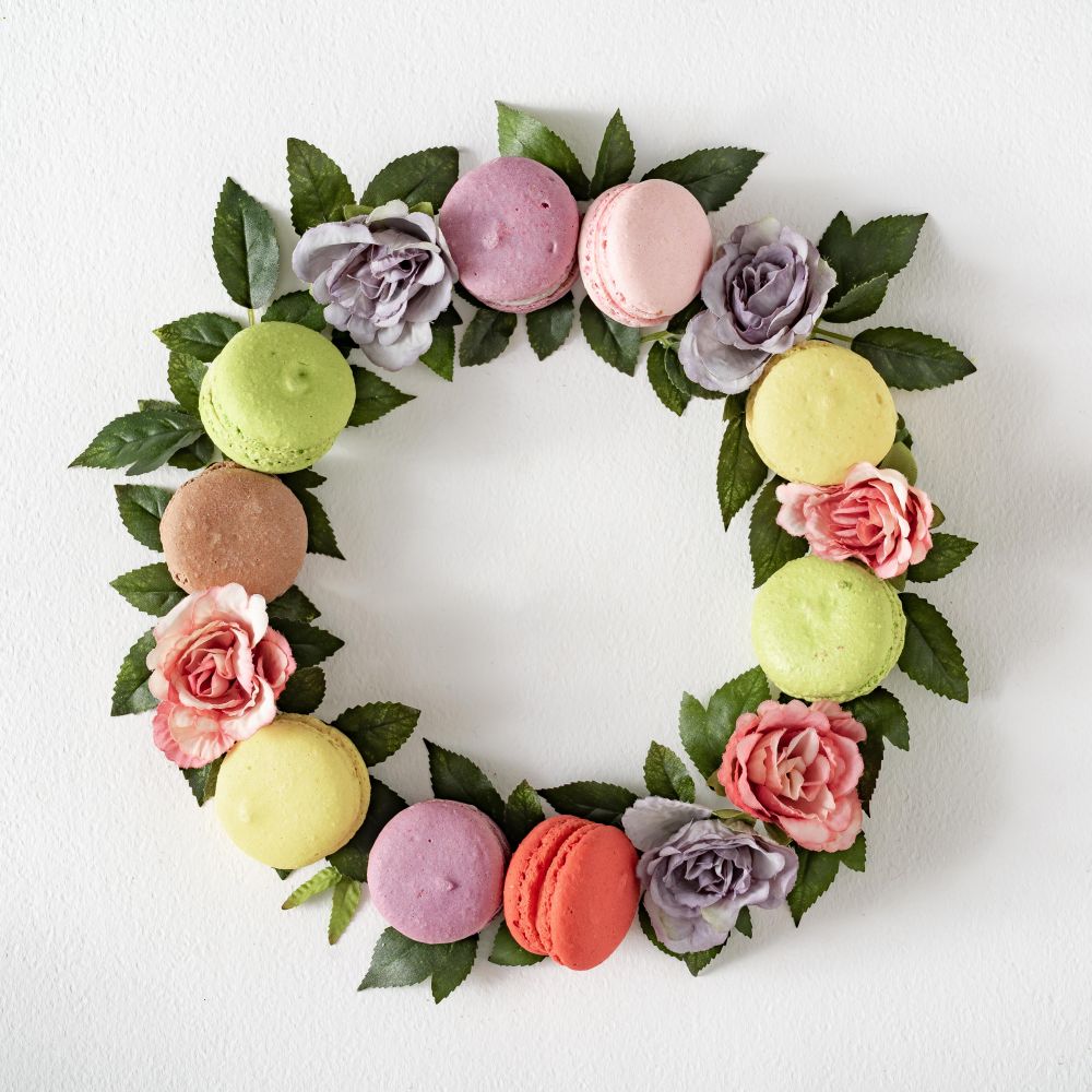 Pink and purple flowers and leaves with macarons in wreath on light  background