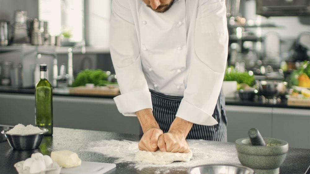 Baker Chef of Famous Restaurant Kneads the Dough in a Modern Looking Kitchen.