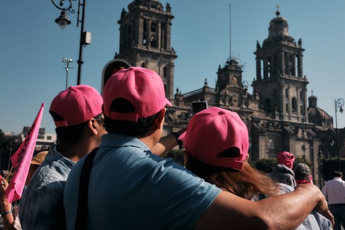 Mexico City, Mexico - February 26th, 2022: Back of three protesters in hats looking up at building