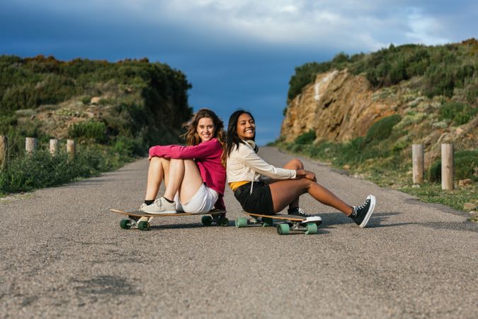 Happy diverse women sitting on longboard on road