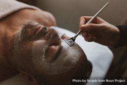 Person applying cream on man's face at spa 5odKg4