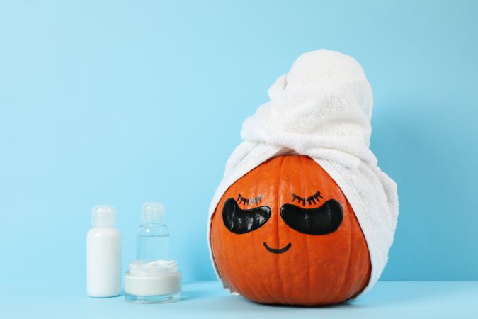 Skincare accessories and pumpkin with eye patches on blue background