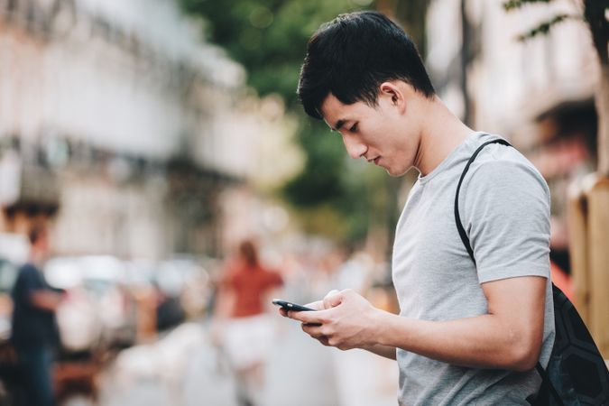 Confused Asian man using smartphone while standing on street