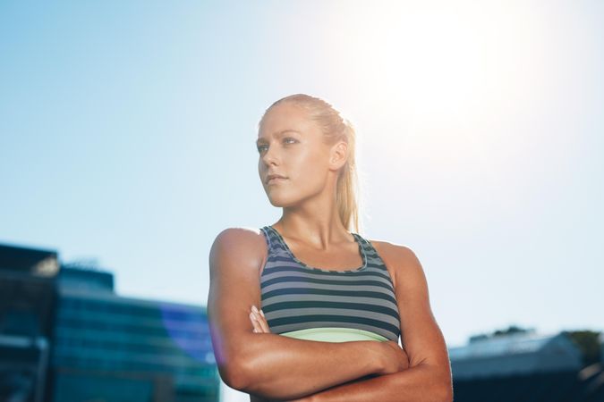 Portrait of a confident young runner standing looking away with her arms crossed