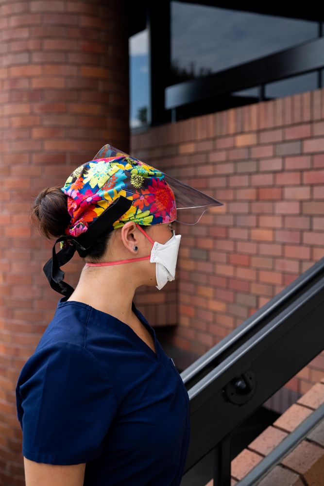 Profile of woman nurse with flowered hair covering, N95 and face shield standing outside