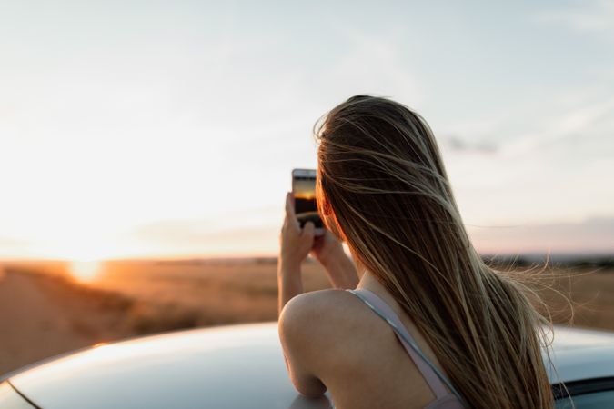 Woman taking a sunset photo form roof of her car