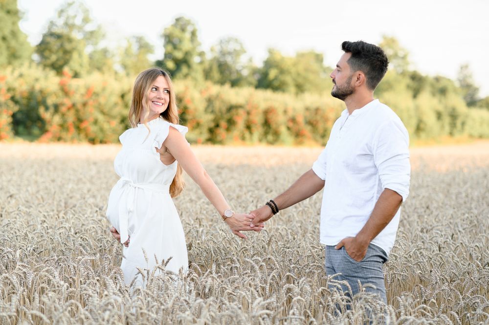 Cheerful expecting couple holding hands while bonding in field